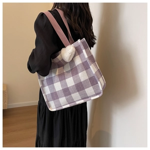 Detail of purple plaid tote bag with white plush heart charm shown on shoulder