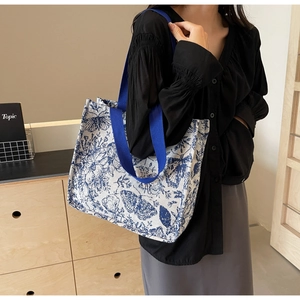 Detail of large canvas tote bag with blue butterfly prints held by a model in black outfit