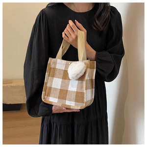 Détail du sac cabas en toile à carreaux avec breloque cœur, tenu par une personne