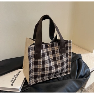 Detail of the woven checkered tote bag with brown fabric handles and golden metal buckle