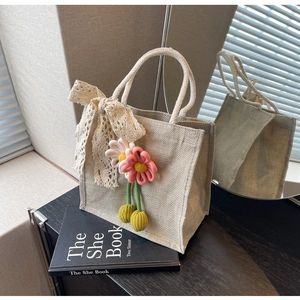 Détail du sac à main tissé beige avec nœud en dentelle et pendentifs fleurs au crochet