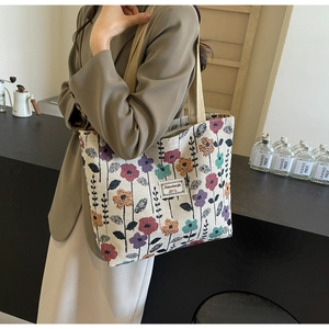 Side view of a beige canvas tote bag with colorful floral embroidery on a female model