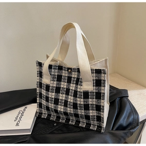 Detailed shot of a woven black and white checkered tote bag with a gold metal clasp