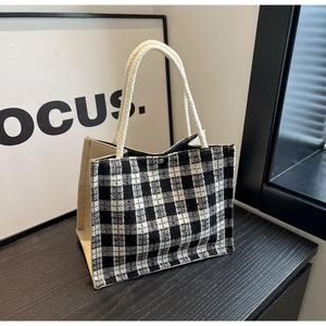 Detail of checkered woven bag with thick rope handles and golden magnetic buckle on wood