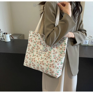 Détail du sac cabas en toile à fleurs avec anses tissées et étiquette sur base beige