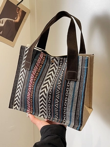 Ethnic woven tote bag with geometric patterns and brown woven handles in a lifestyle setting