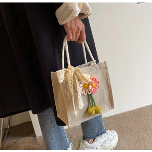 Détail du sac en lin avec un nœud en dentelle beige et des breloques florales 3D