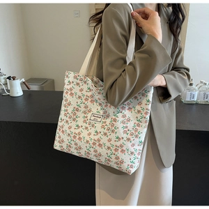Détail du cabas en toile florale avec large bandoulière et étiquette en cuir sur l'épaule