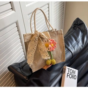 Détail du sac en jute avec nœud en dentelle blanche et breloques de fleurs cerises au crochet