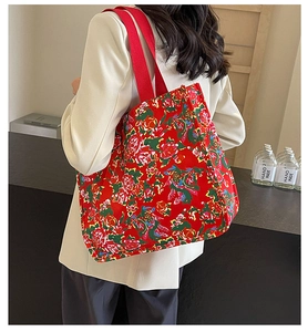 Detail of large floral canvas tote bag with red handles shown on shoulder with blazer