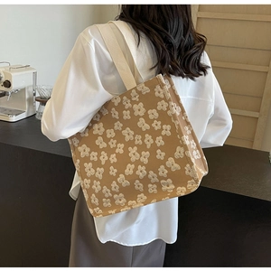 Brown canvas tote bag with white 3D floral pattern worn by a model in a cafe setting