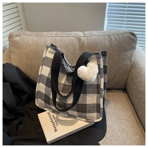 Détail d'un sac cabas à damier avec anses tissées et breloque coeur sur un canapé