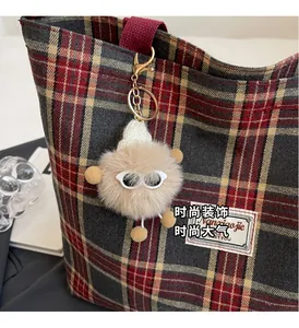 Detail of creative plush monster keychain with sunglasses on a red plaid canvas tote bag