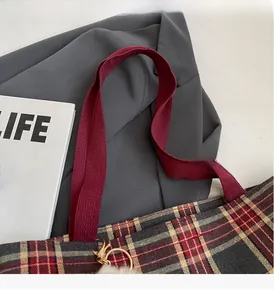 Close-up of tartan canvas tote with burgundy woven handles and golden metal rings