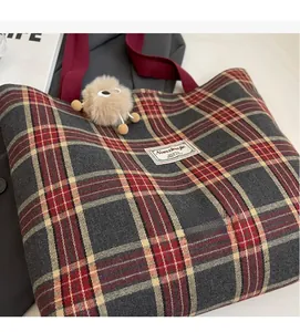 Detail of red and grey plaid canvas tote bag with a brown plush monster charm attached