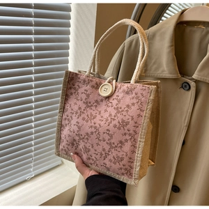 Dettaglio di borsa tote in juta floreale con bottone beige e manici in corda intrecciata