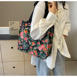 Detailed view of a black floral tote bag with vibrant red and yellow blooms on shoulder