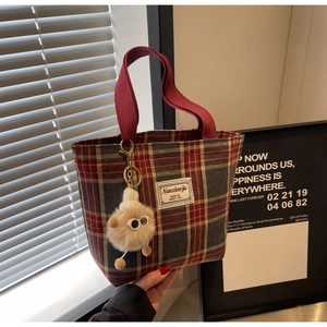 Detail of plaid canvas tote bag with red handles and furry ball charm accessory