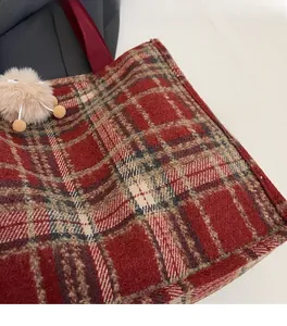 Close-up of red plaid wool fabric texture and soft pompom charm on a tote bag