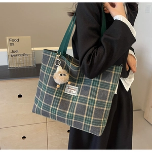 Detail of green plaid canvas tote bag with plush charm and woven top handles