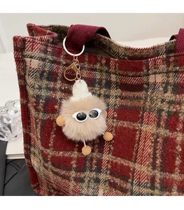 Close-up of a plush cartoon doll pendant with sunglasses hanging on a brown plaid tote bag