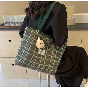 Detail of green plaid canvas tote bag featuring a cute fuzzy monster keychain and long straps