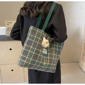 Retro plaid canvas tote bag with plush monster charm worn by a model in a minimal setting