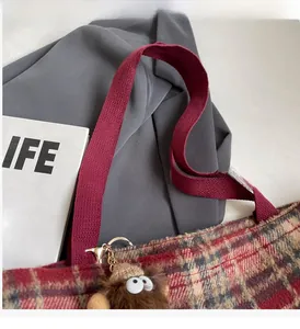 Détail d'un sac cabas en tweed à carreaux rouges avec anses tressées et charme peluche