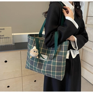 Close-up of a green plaid canvas tote bag with a cute plush charm and fabric strap