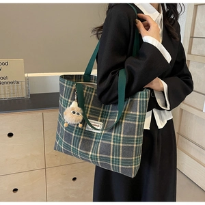Detail of green and grey checkered canvas tote bag with a plush doll charm on shoulder
