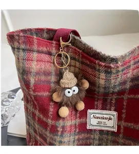 Détail d'un porte-clé monstre en peluche sur un sac cabas à carreaux rouges et or