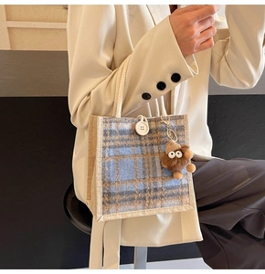 Detail of blue and brown checkered tote bag with white button and plush monster charm