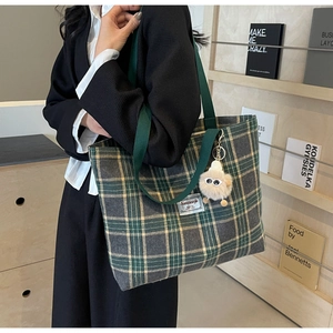 Detail of grey-green plaid tote bag with plush monster charm and canvas straps