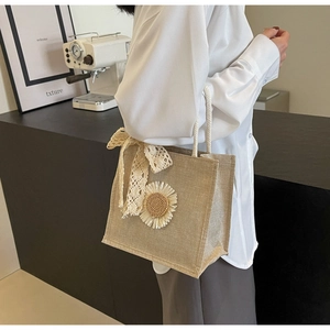Detail of natural linen handbag featuring daisy embroidery and white lace bow decoration