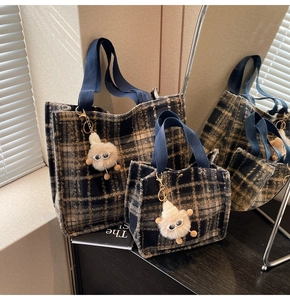 Detail of checkered woolen tote bags with blue canvas handles and a plush monster charm