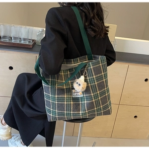 Detail of green plaid canvas tote bag with shoulder straps and plush monster charm