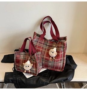 Close-up of red plaid tweed tote bags with plush monster charms and webbed handles