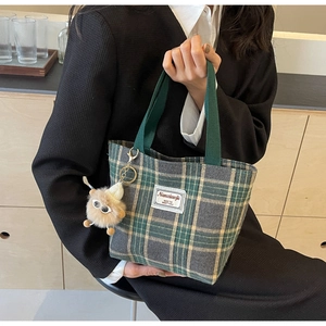 Detail of plaid canvas tote bag with monster charm and branded woven label decoration