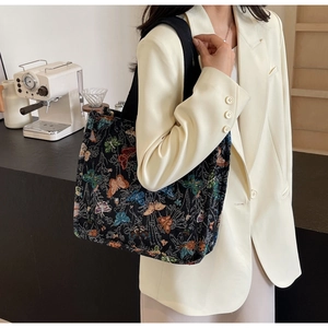 Detail of a large canvas tote bag with colorful butterfly embroidery worn by a model