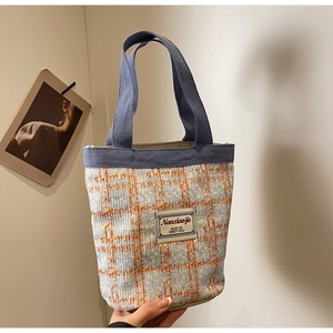 Close-up of blue and white tweed bucket bag with orange checks and woven handle