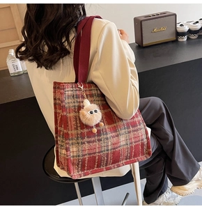 Close-up of red plaid tweed tote bag with plush charm and wide fabric shoulder strap
