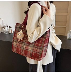 Detail of red plaid tweed tote bag with plush charm on model in a white blazer