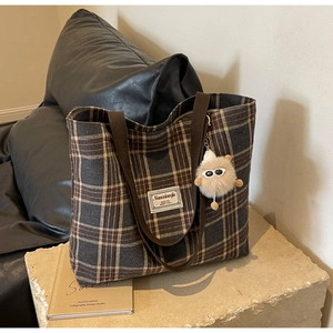 Close-up of brown plaid tweed tote bag with textured brand label and plush monster charm