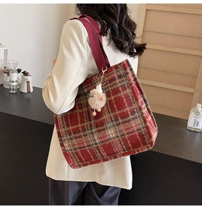 Detail of red-brown plaid wool tote bag with soft plush charm and wide fabric strap