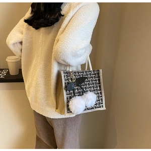 Gros plan du sac à déjeuner en lin avec tissage à carreaux et breloques pompons blancs