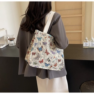 Detail of a beige canvas tote with colorful butterfly prints and wide shoulder strap