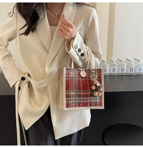 Detail of red plaid tote bag with decorative button and plush doll on beige blazer