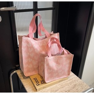 Detail view of two pink canvas tote bags with white heart patterns in two sizes