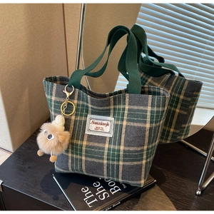 Close-up of plaid canvas tote bag with a brown plush charm and brand label on a desk