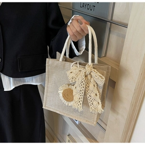 Detail of woven jute tote bag with white lace bow and sunflower accent decoration